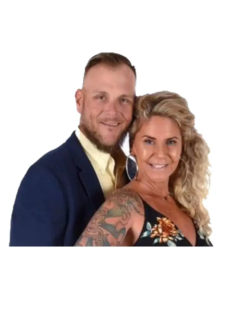 about own image webp A man in a dark suit and a woman in a floral dress pose closely together, showcasing the woman’s intricate tattoos.